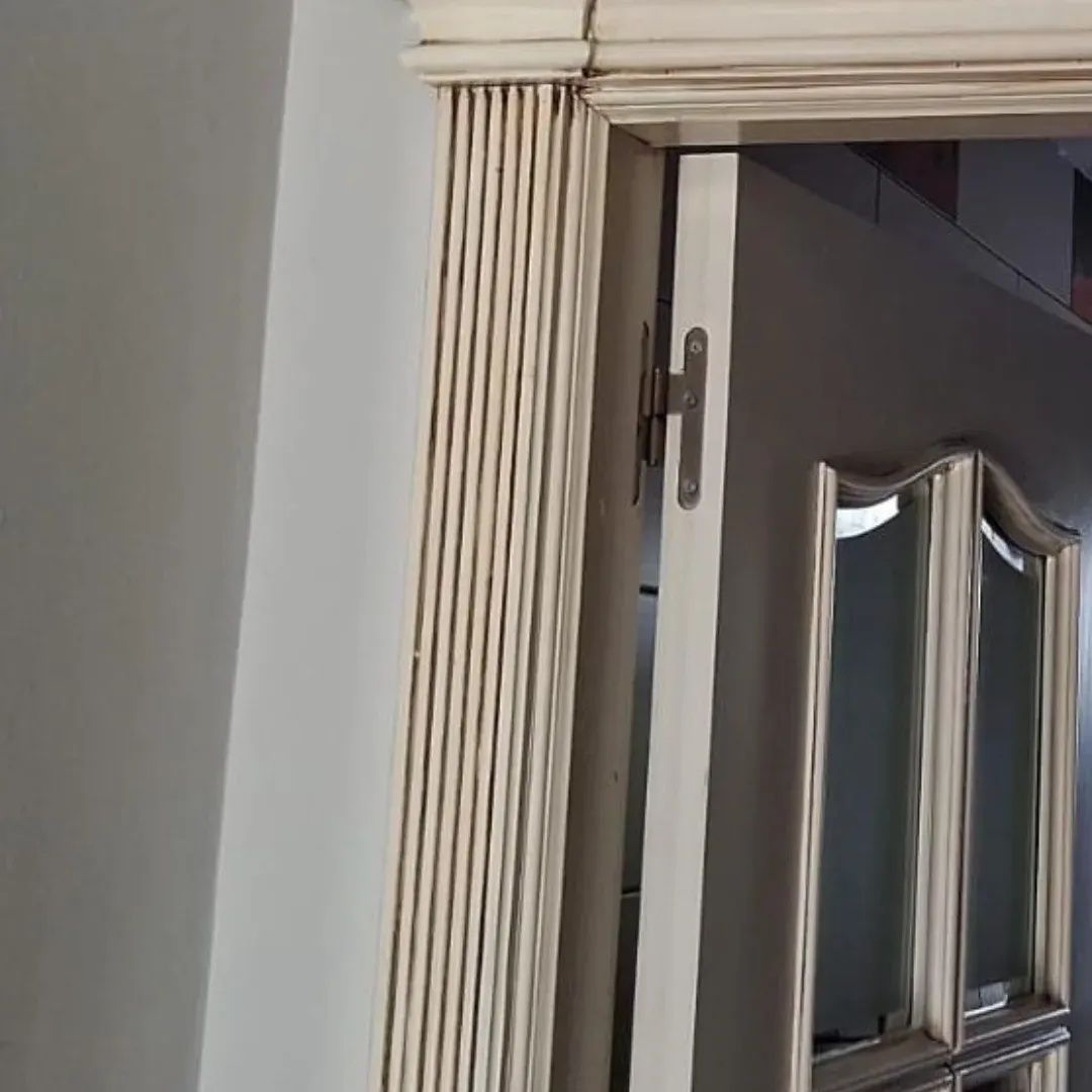 Marco de puerta blanco junto a una puerta abierta, con un armario con espejo visible en la habitación contigua.