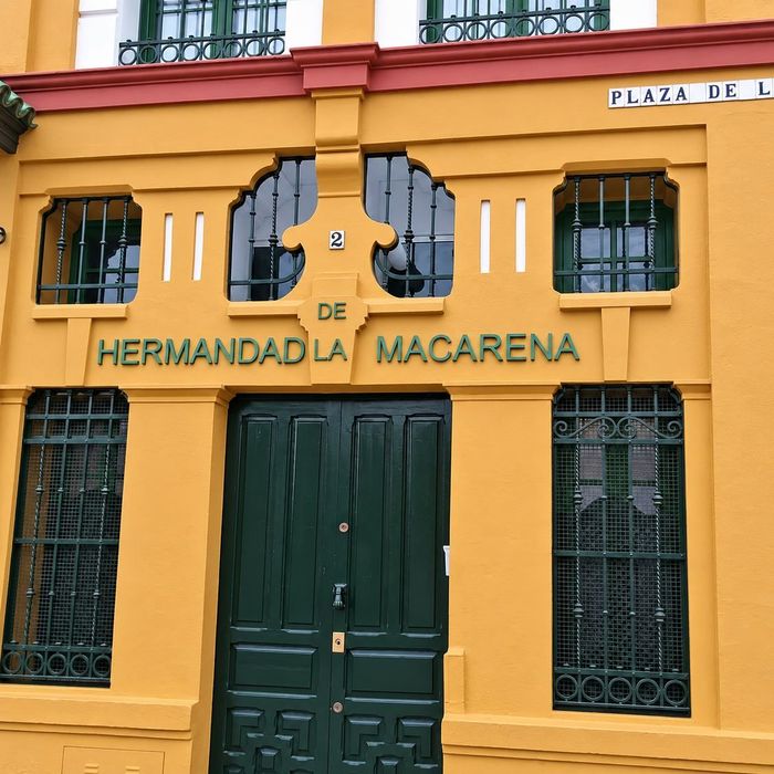 Fachada amarilla de la Hermandad de la Macarena, con puertas verdes y ventanas enrejadas