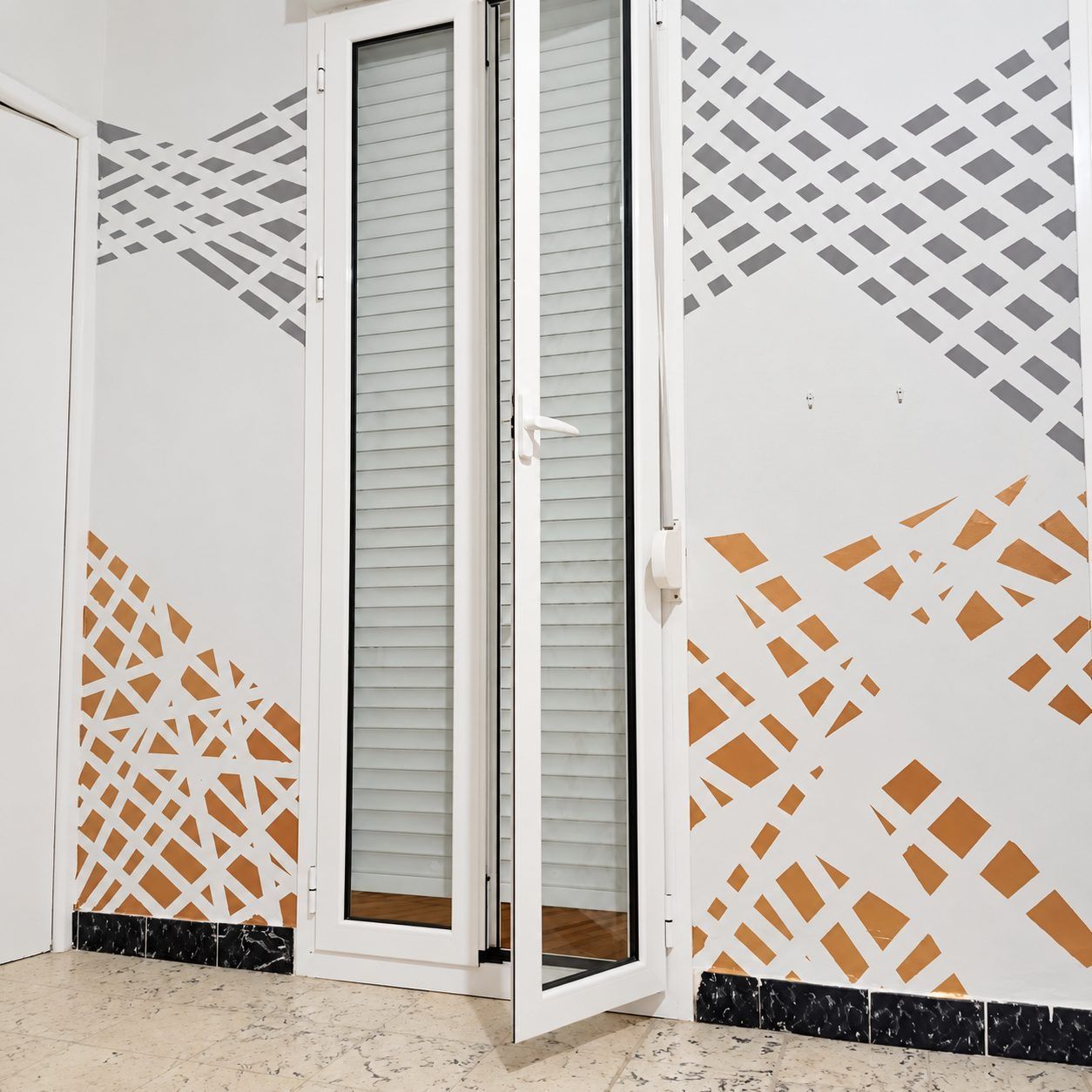 Abre una puerta blanca con paneles de vidrio en un pasillo, decorado con patrones geométricos grises y naranjas en las paredes