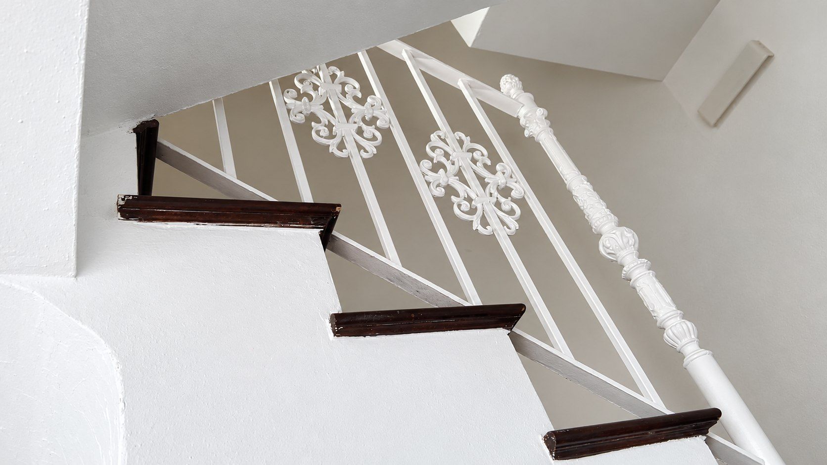 Escalera blanca con peldaños de madera oscura y barandillas blancas decorativas, vista desde abajo