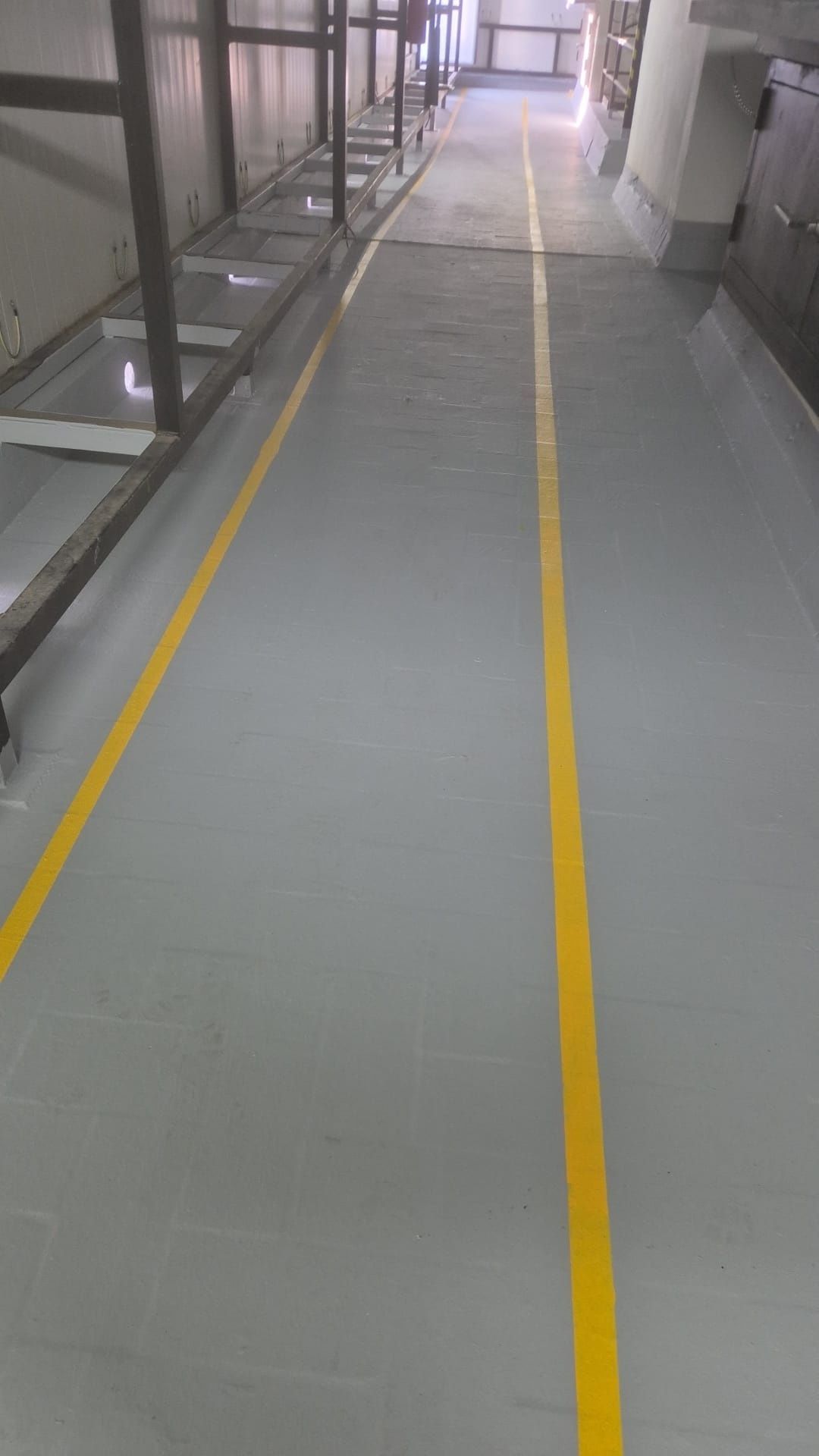 Pasillo interior con dos líneas guía amarillas pintadas sobre un suelo gris.
