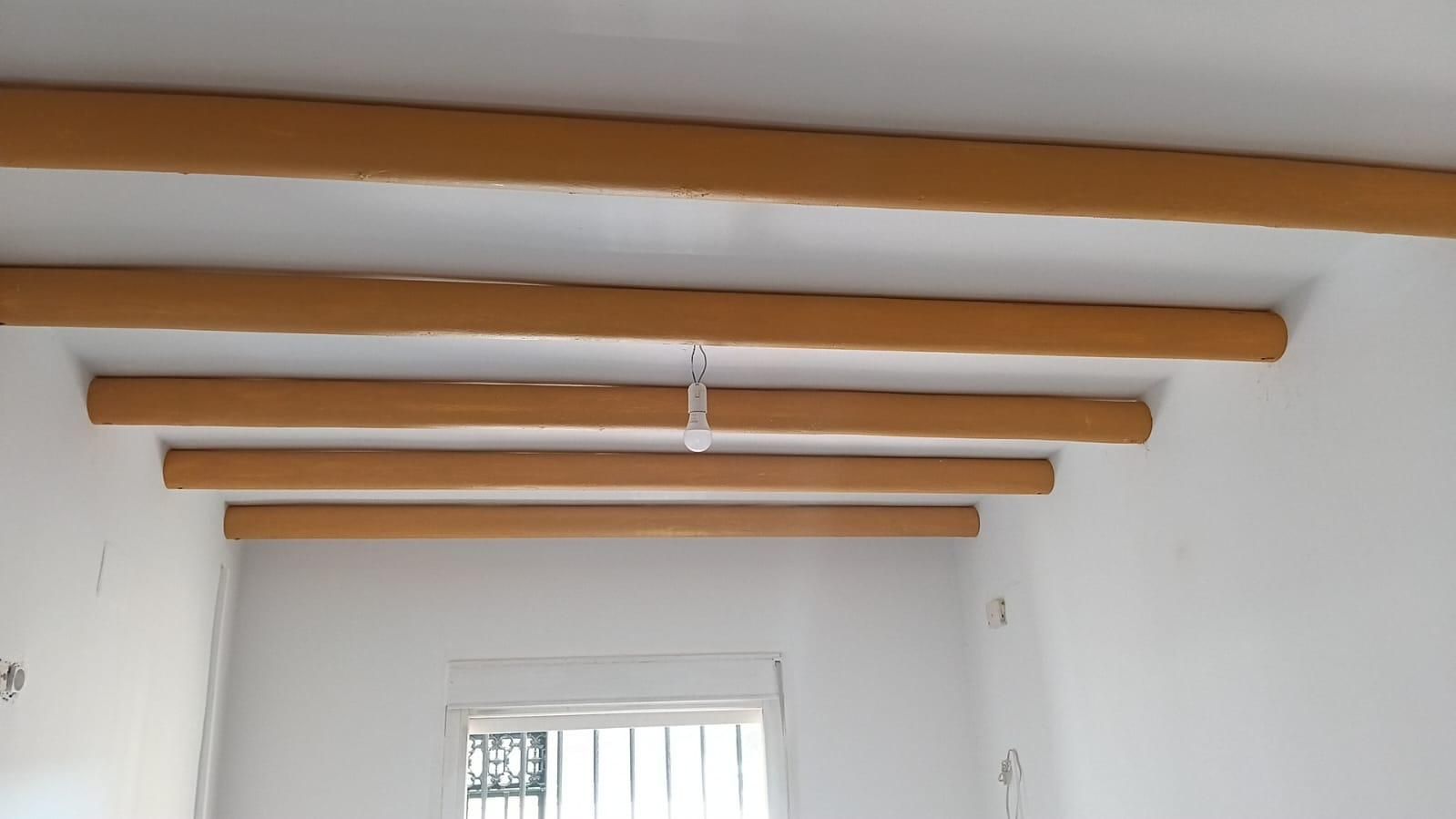 Techo blanco de una habitación con vigas de madera a la vista sobre una ventana