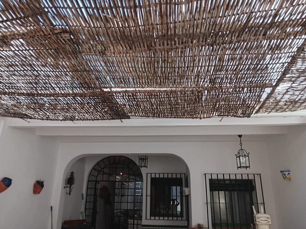 Patio con paredes blancas y ventanas arqueadas bajo un tejado de sombra de bambú trenzado