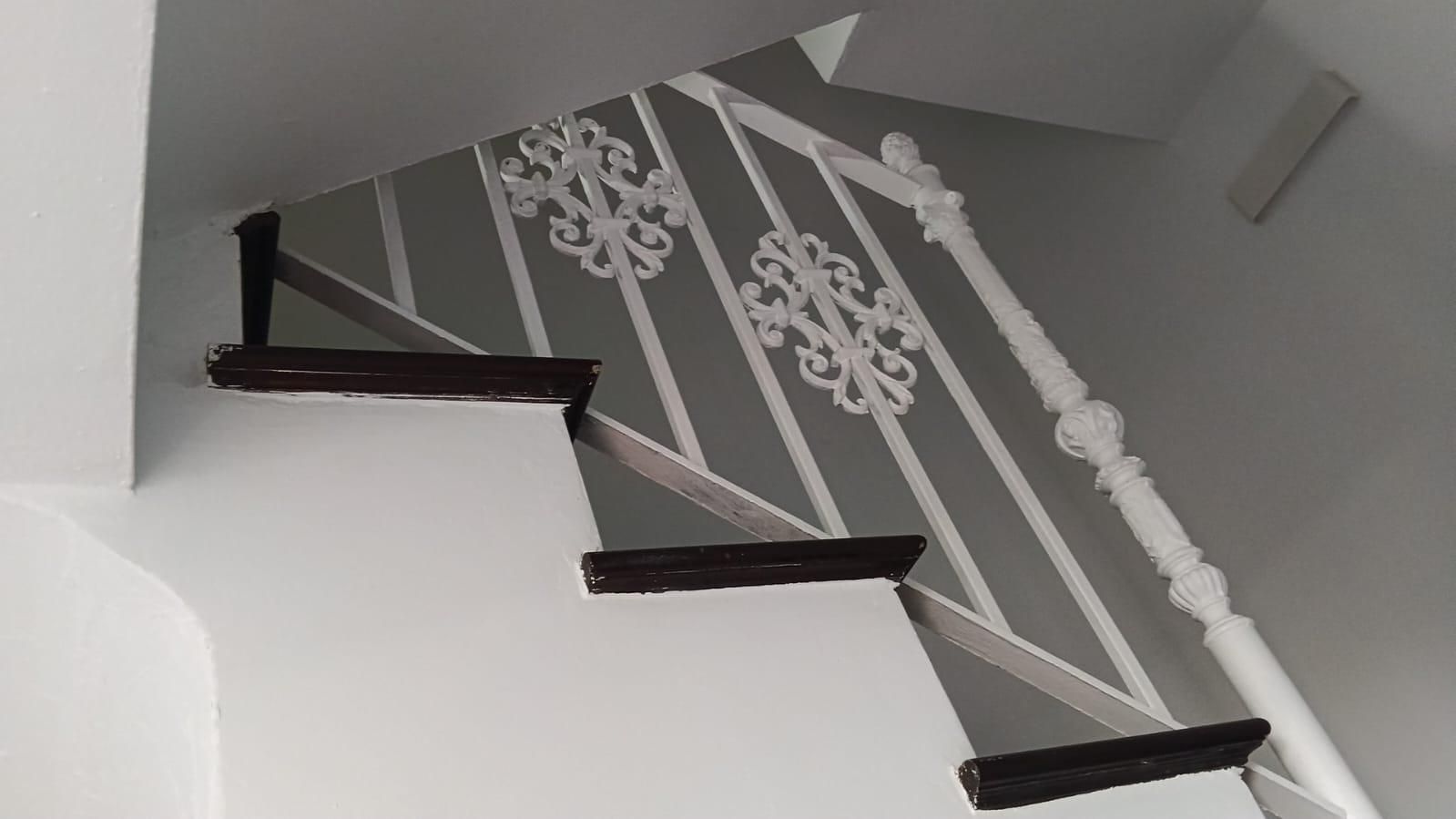 Escalera interior blanca con peldaños de madera oscura y detalles decorativos en la barandilla blanca