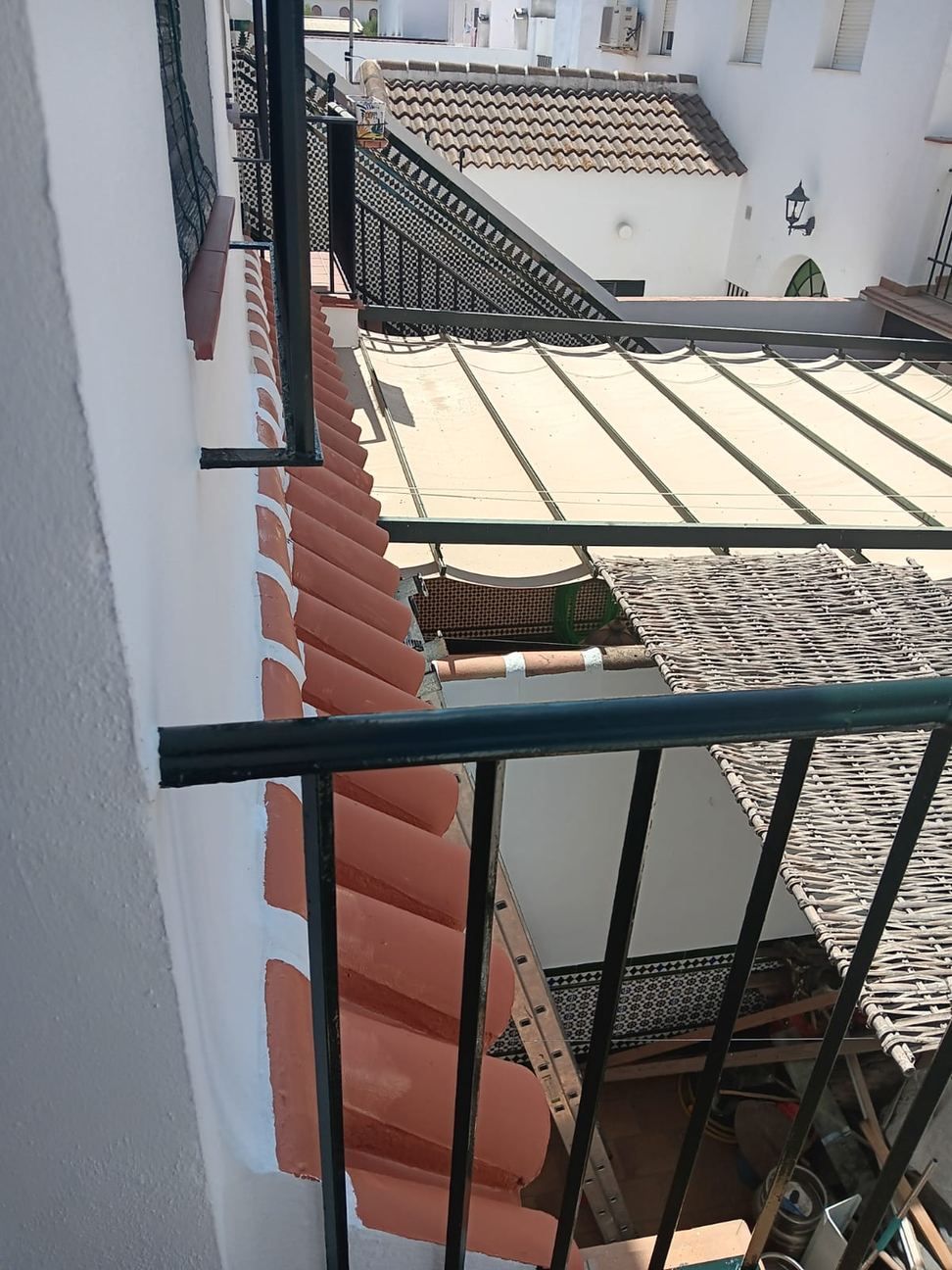 Vista estrecha de edificios blancos, tejas rojas y barandillas de hierro negro en un patio soleado