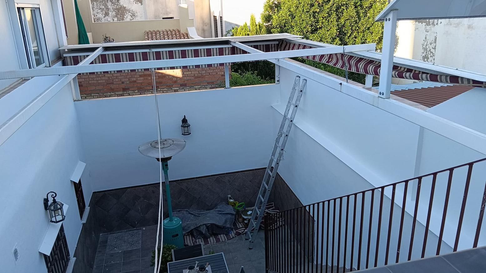 Patio blanco con barandilla, fuente y escalera que conduce a un patio superior bajo una pérgola