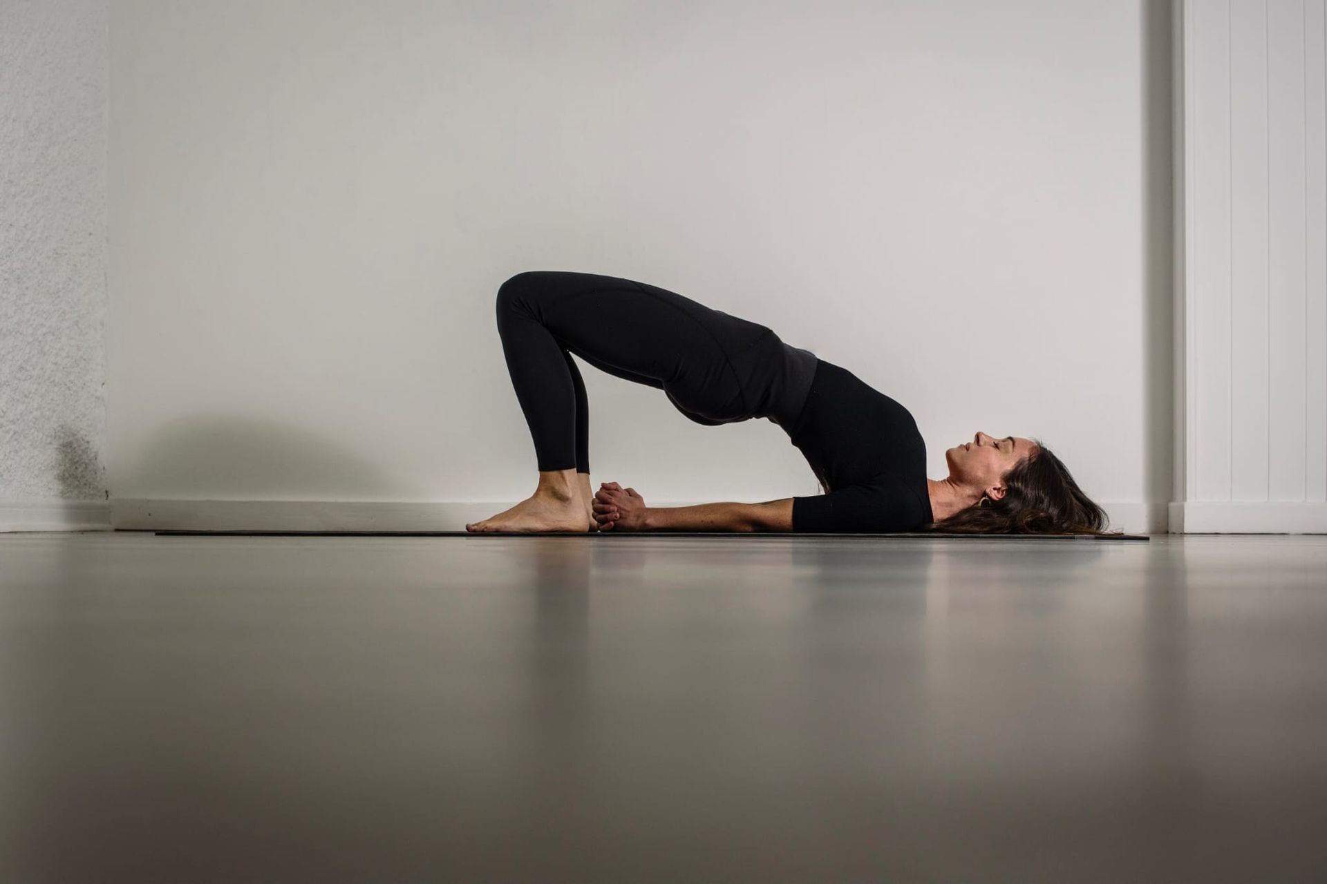 Persona realizando la postura del puente sobre una esterilla de yoga en una habitación minimalista.