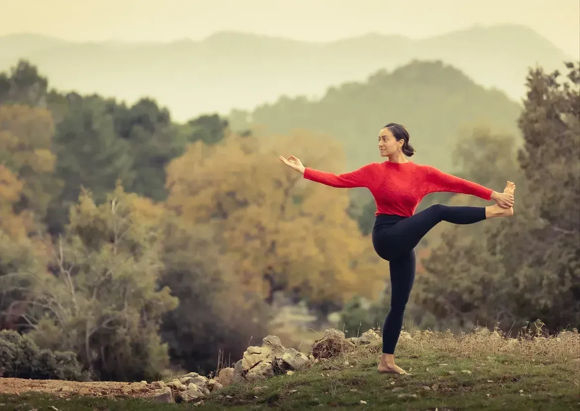 Una persona con una blusa roja se mantiene en equilibrio al aire libre con los brazos extendidos 