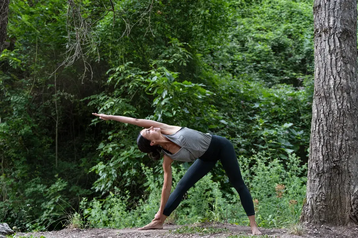 Una persona se estira haciendo flexiones laterales en un claro del bosque verde cerca de un árbol.