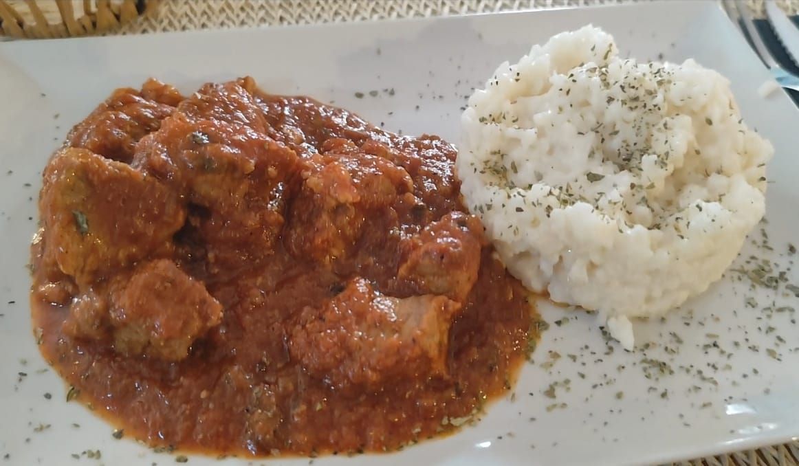 Pollo en salsa de tomate con acompañamiento de arroz blanco, espolvoreado con hierbas, en un plato blanco.