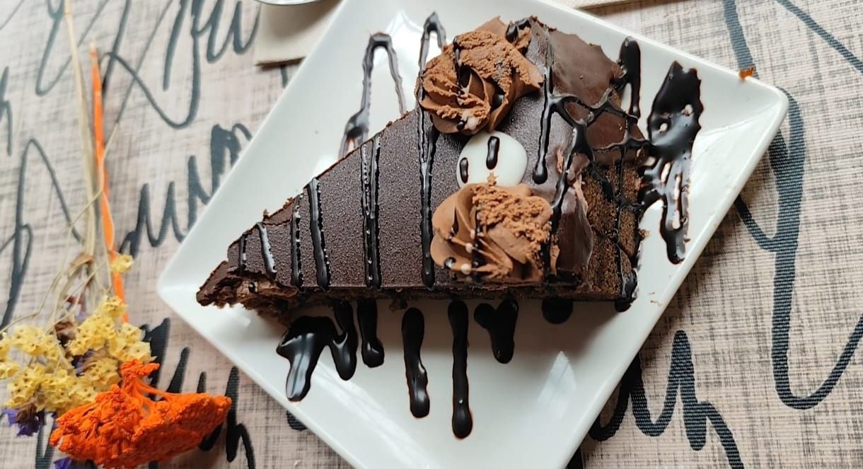 Rebanada de pastel de chocolate con salsa de chocolate y glaseado, en un plato cuadrado blanco.