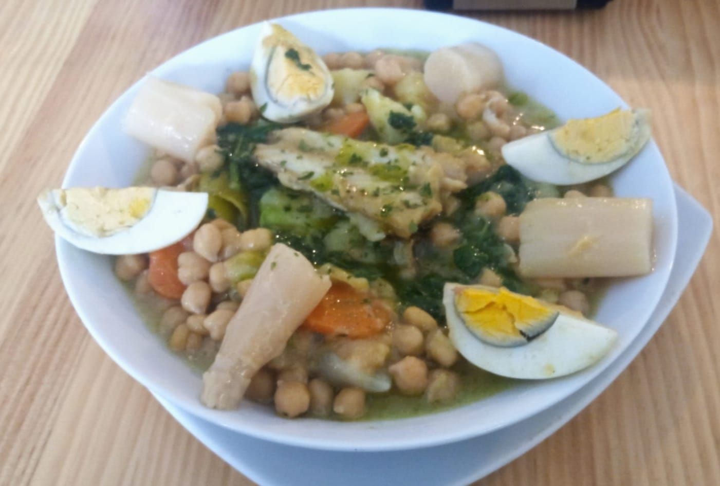 Plato de guisado con garbanzos, pescado, verduras y huevos cocidos.