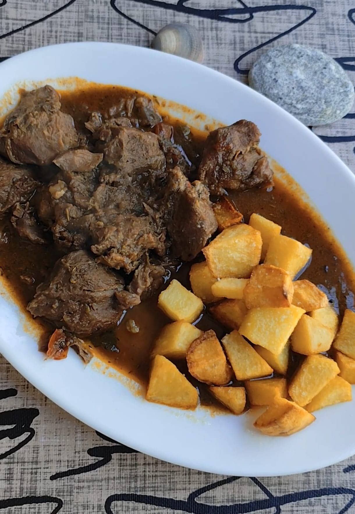 Carne guisada con patatas fritas en un plato blanco. Guiso marrón, patatas doradas.