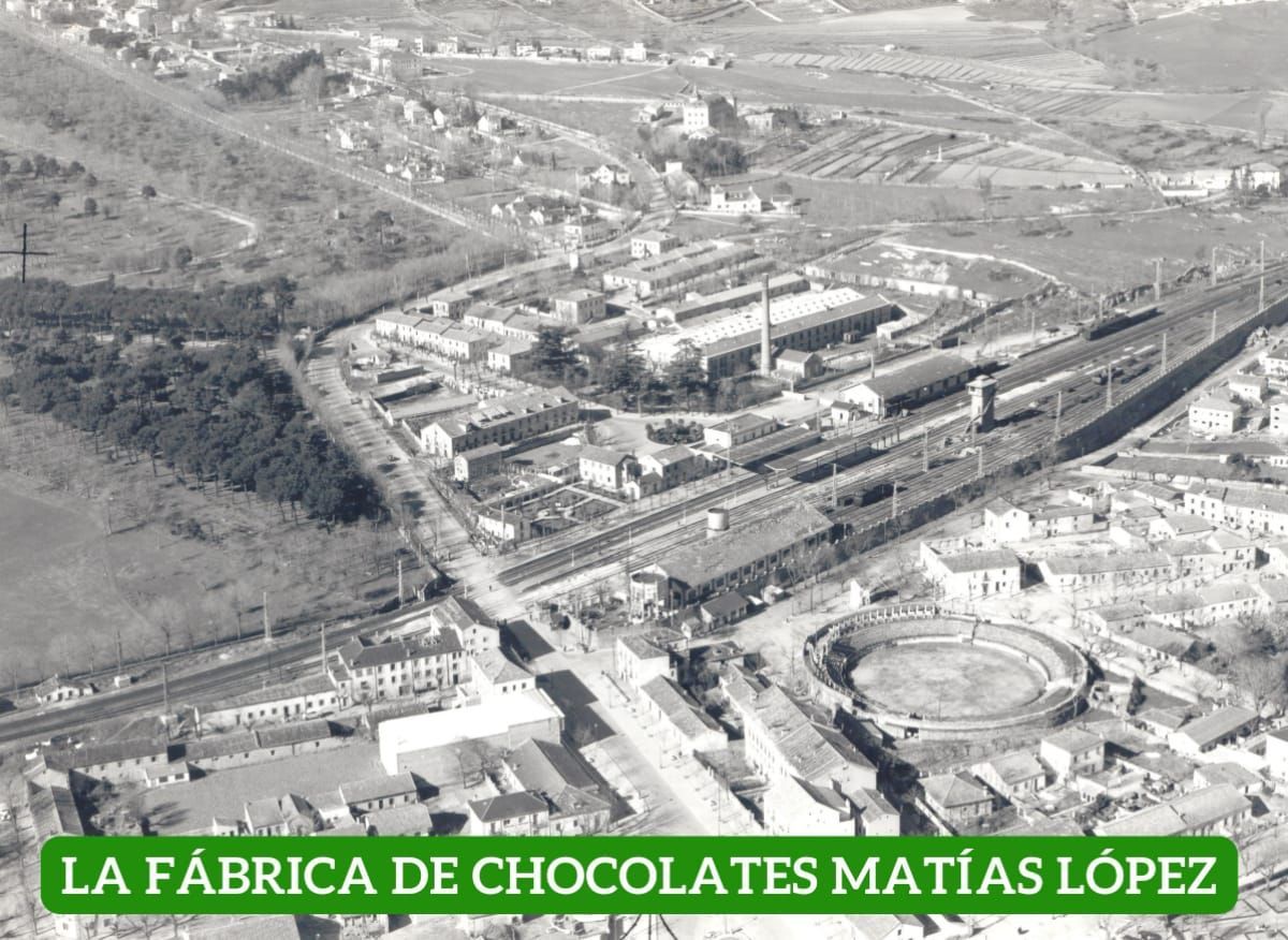 Vista aérea de una fábrica de chocolate, vías de tren y una plaza de toros en una ciudad.