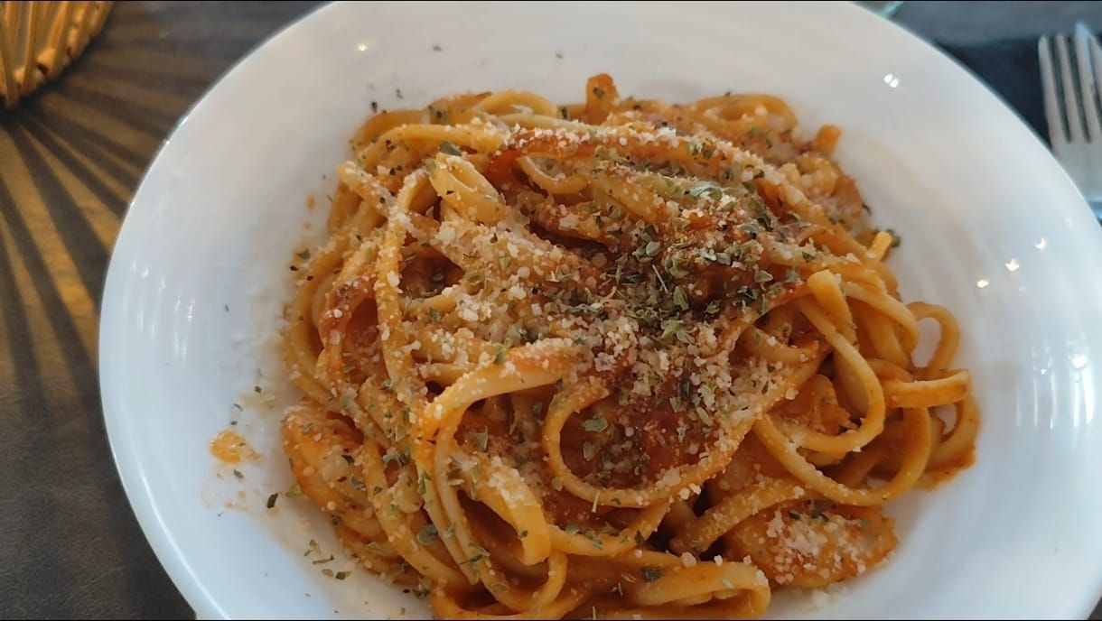 Pasta linguini en salsa de tomate cremosa, adornada con hierbas y parmesano, en un tazón blanco.