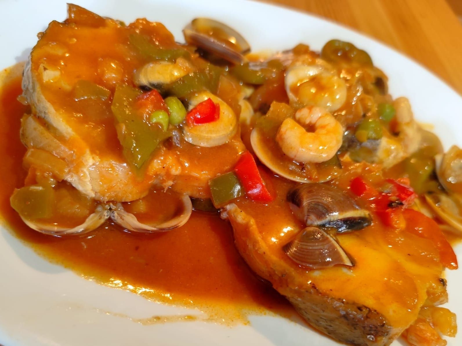 Guiso de pescado con camarones, almejas y verduras en salsa de color naranja rojizo.