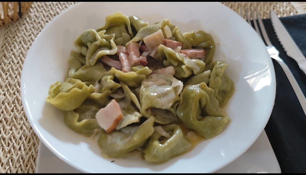 Pasta tortellini verde con jamón en salsa cremosa, servida en un plato blanco.
