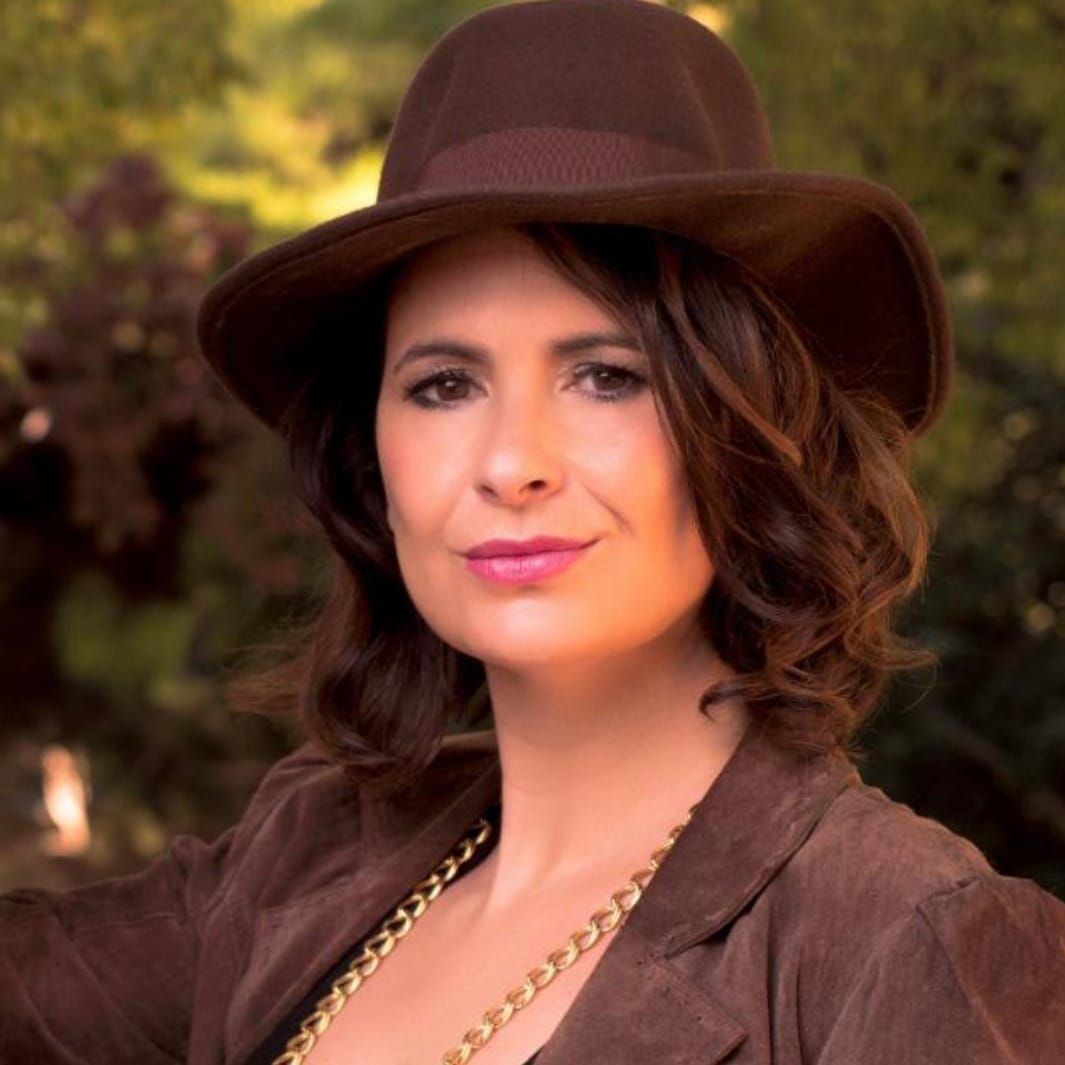 Interior de una cafetería con gente sentada a las mesas. Paredes azules, mesas de madera clara y una decoración floral en la pared.