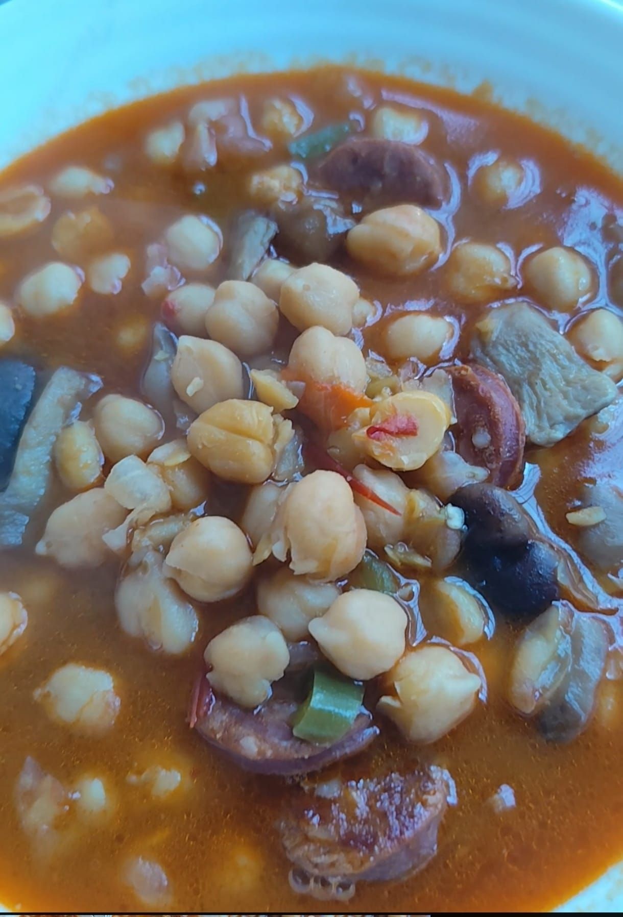 Guiso de garbanzos con chorizo, verduras y carne en caldo marrón.