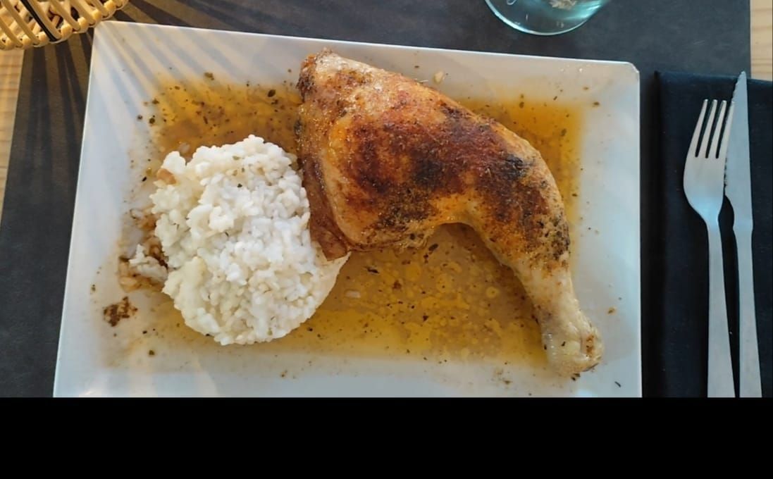 Muslo de pollo asado y arroz en un plato blanco con cubiertos.