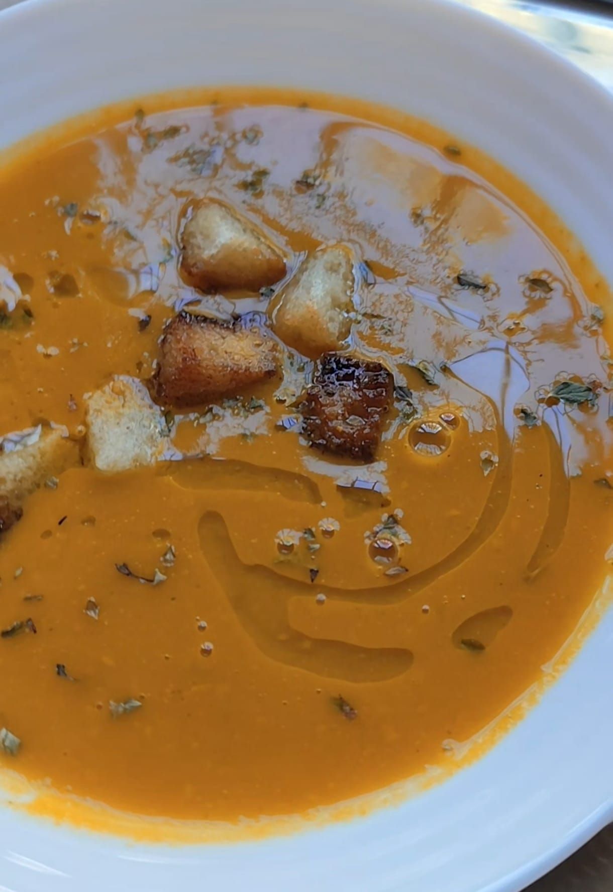 Sopa de naranja en un recipiente blanco, adornada con crutones y un chorrito de aceite de oliva.