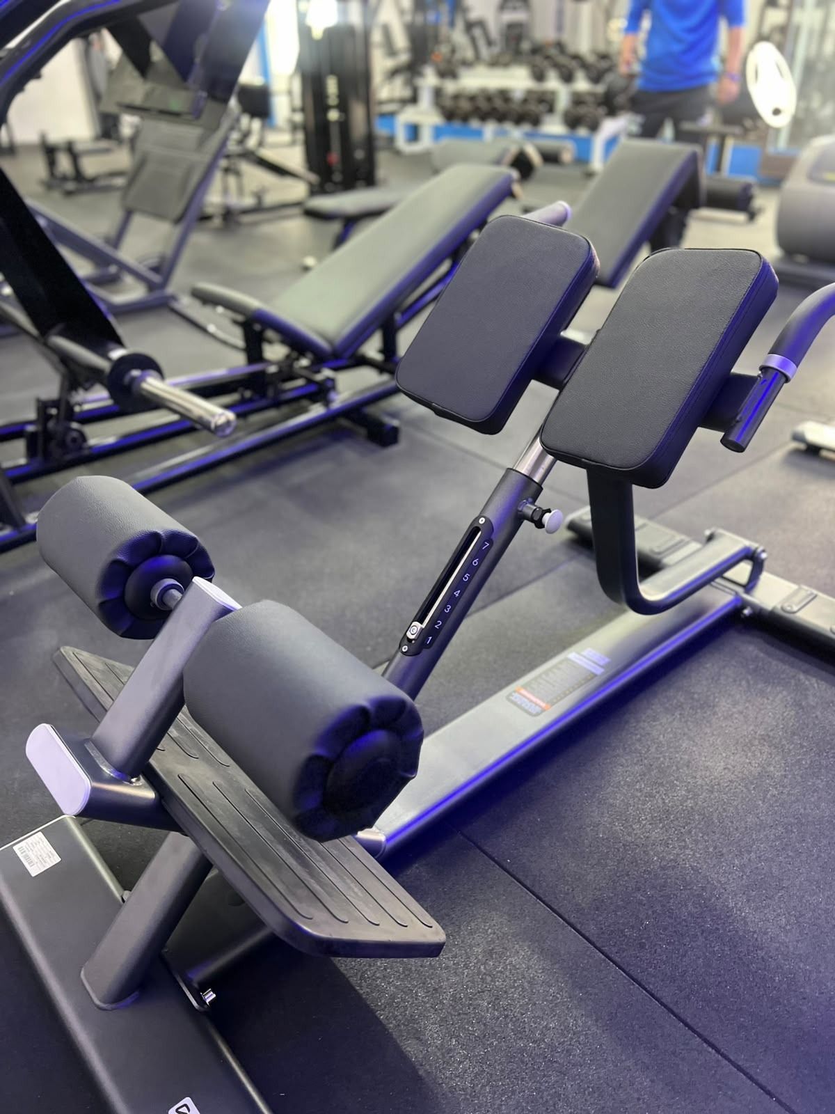 Máquina negra de curl de piernas en un gimnasio, con rodillos acolchados y respaldos inclinados
