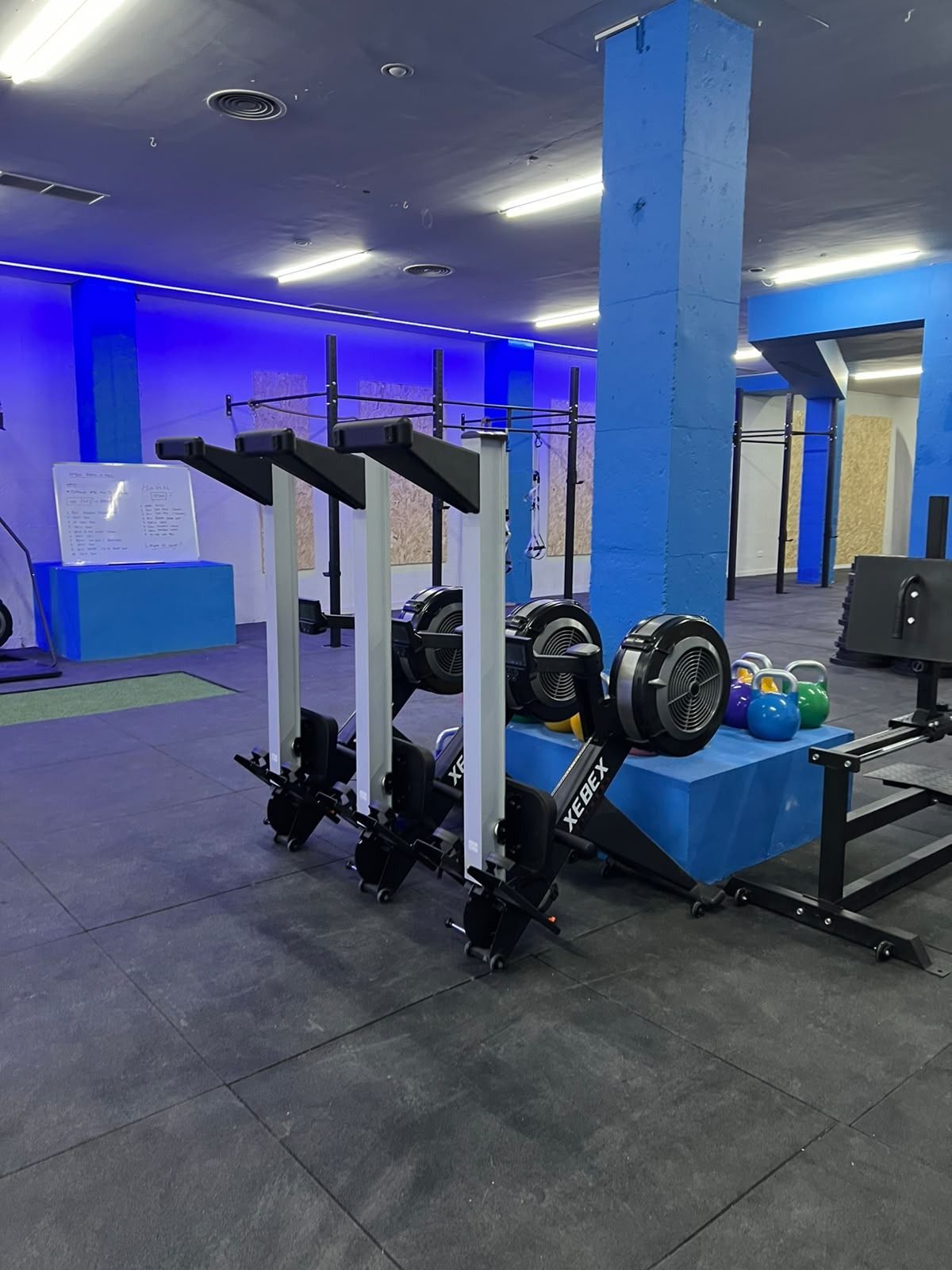 Interior de un gimnasio con trineos de pesas, neumáticos e iluminación azul