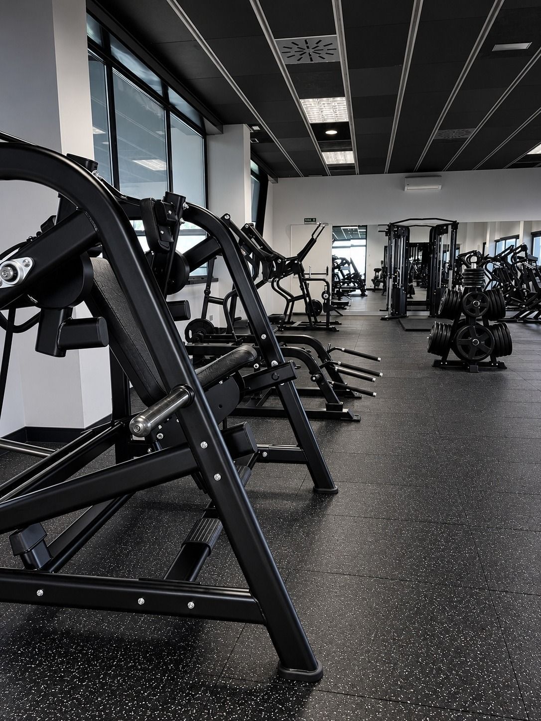 Gimnasio moderno y vacío, con máquinas de cardio negras, paredes con espejos y suelo moteado.