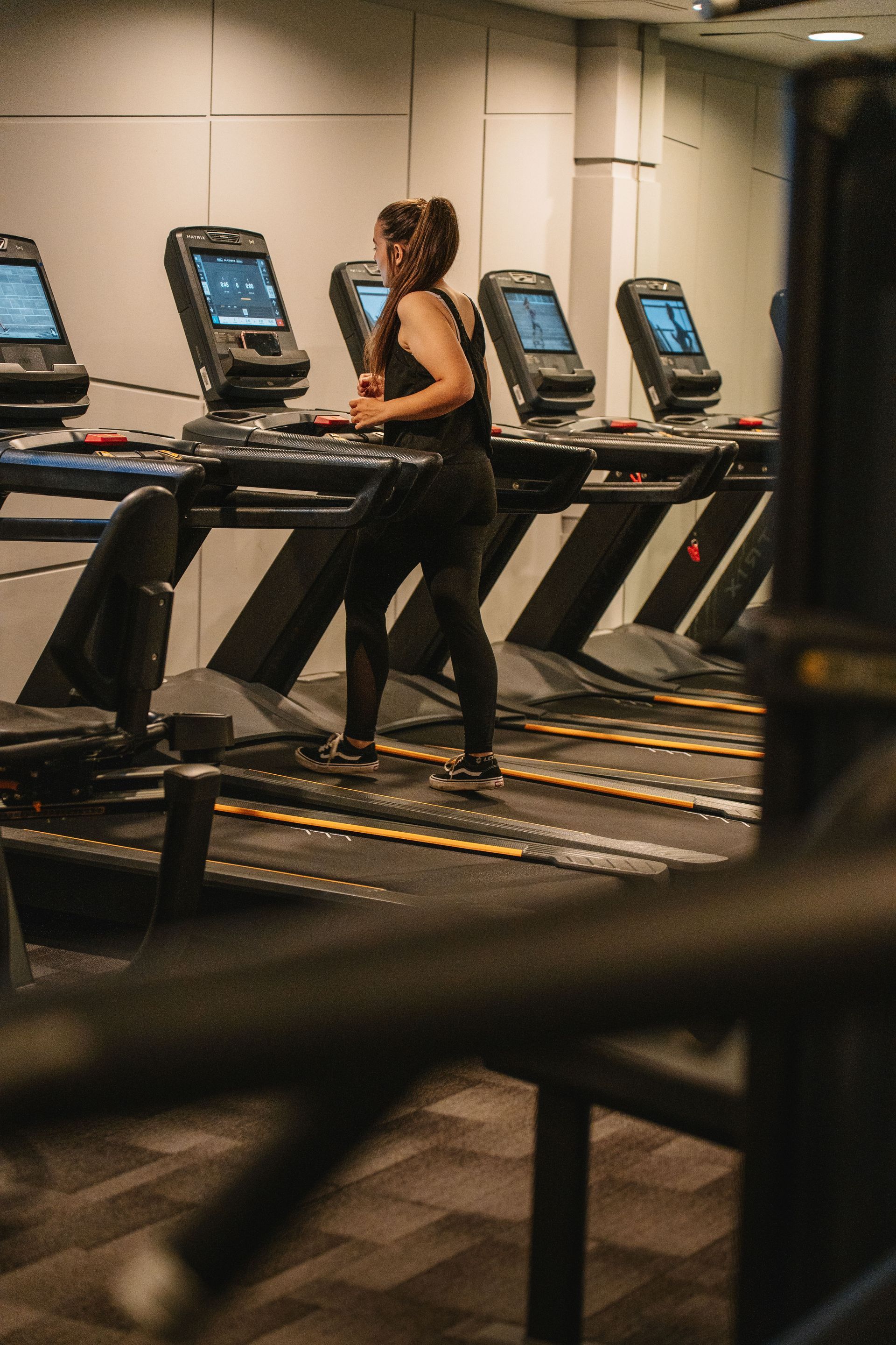 Una persona corriendo en una cinta de correr en un gimnasio, vista desde atrás, con varias cintas alineadas.