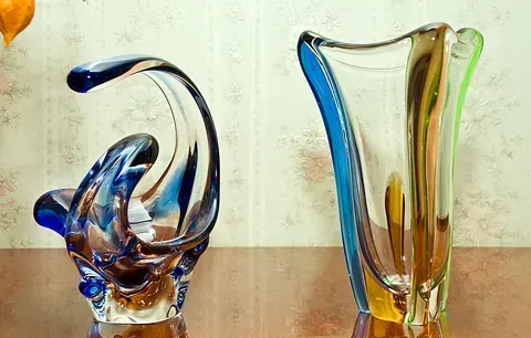 Dos jarrones de cristal de colores están sobre una mesa de madera.