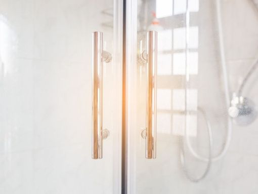Un primer plano de una puerta de ducha con dos manijas en un baño.