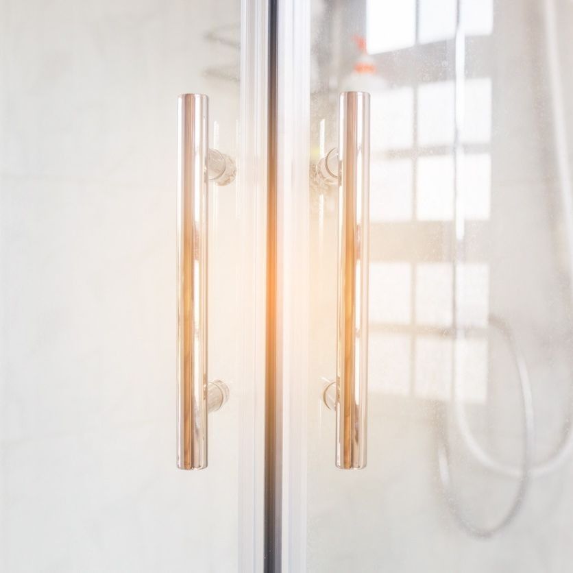 Un primer plano de una puerta de ducha con manijas de acero inoxidable en un baño.