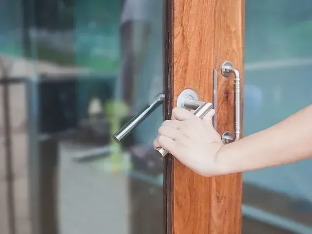 Una persona está abriendo una puerta de vidrio con manija de madera.