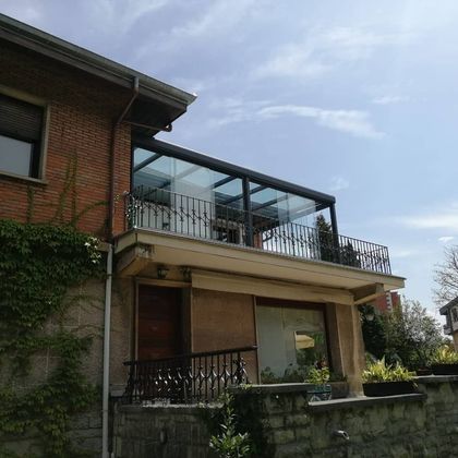Una casa de ladrillo con un balcón de cristal encima.