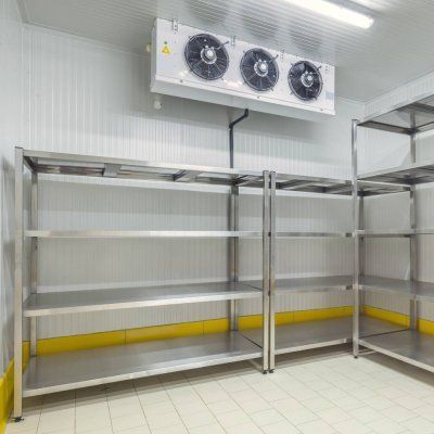 Tyhjä kylmävarasto, jossa on metallihyllyt ja seinälle asennetut jäähdytyspuhaltimet