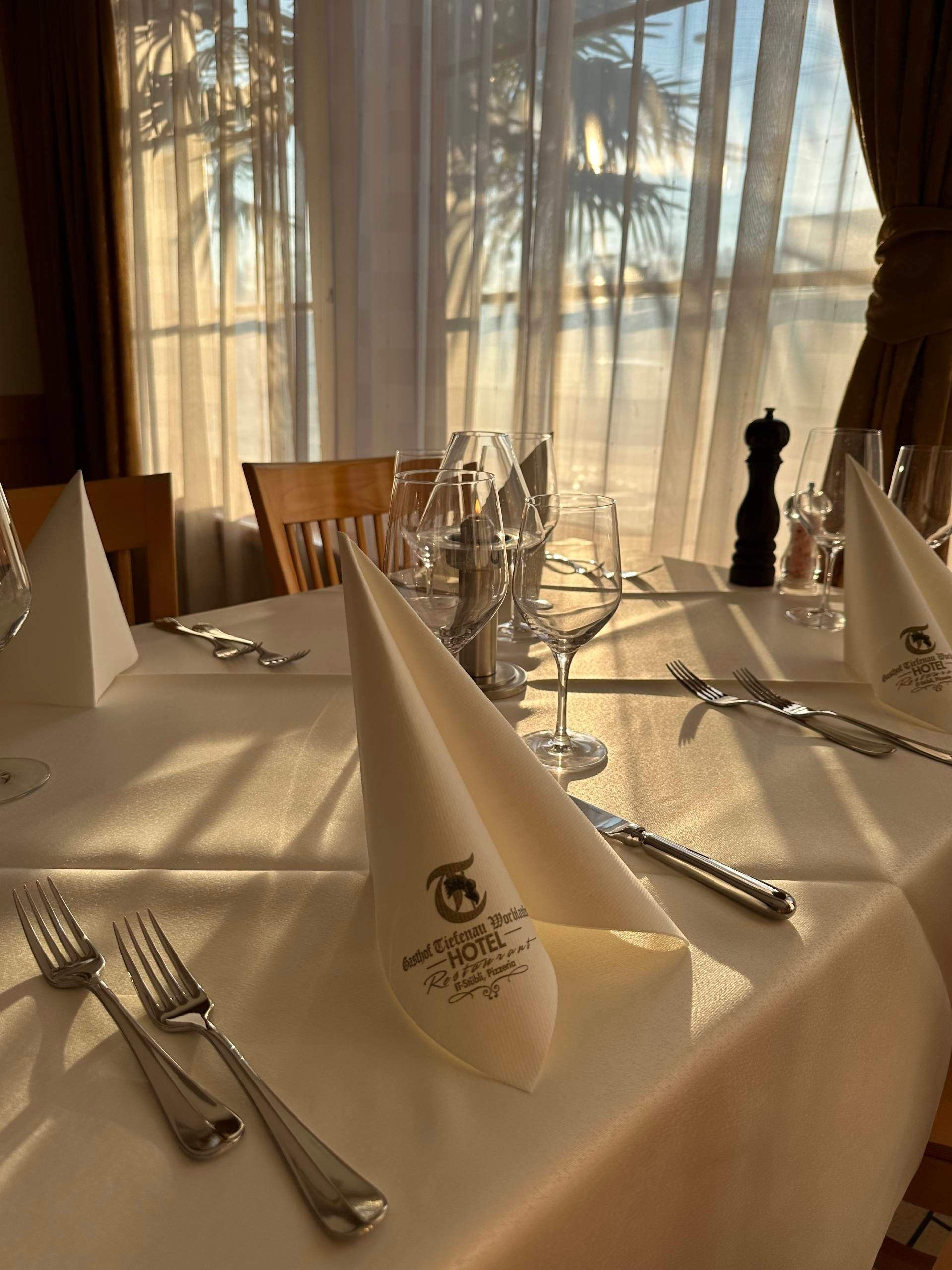 Ein zum Essen gedeckter Tisch, sonnenbeschienen mit gefalteten Servietten und Besteck, in einem Restaurant in der Nähe eines Fensters.