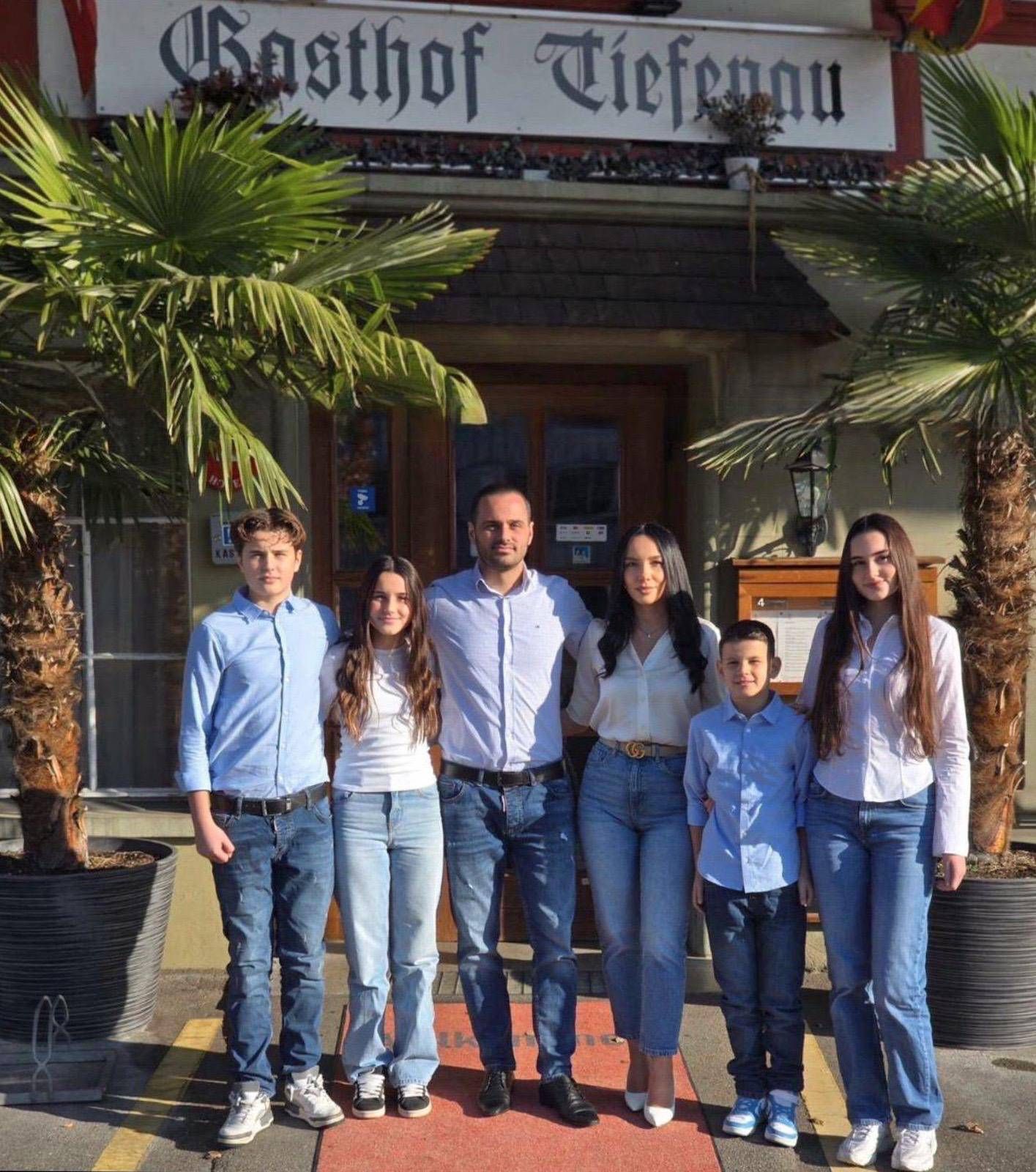 Eine sechsköpfige Familie steht vor dem Restaurant „Gasthof Tiefenau“. Die Personen tragen Jeans und helle Oberteile.