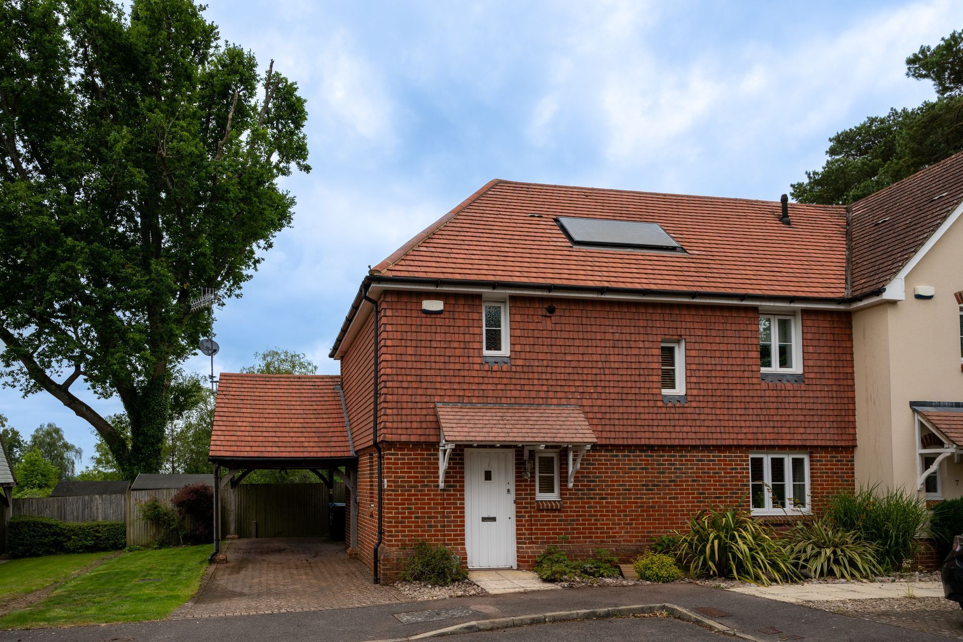 Red-brick house with a red tiled roof, white door, and attached carport under a cloudy sky.