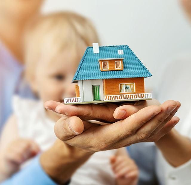 Une famille tenant une maison miniature, symbolisant peut-être la propriété d'un logement ou la sécurité.