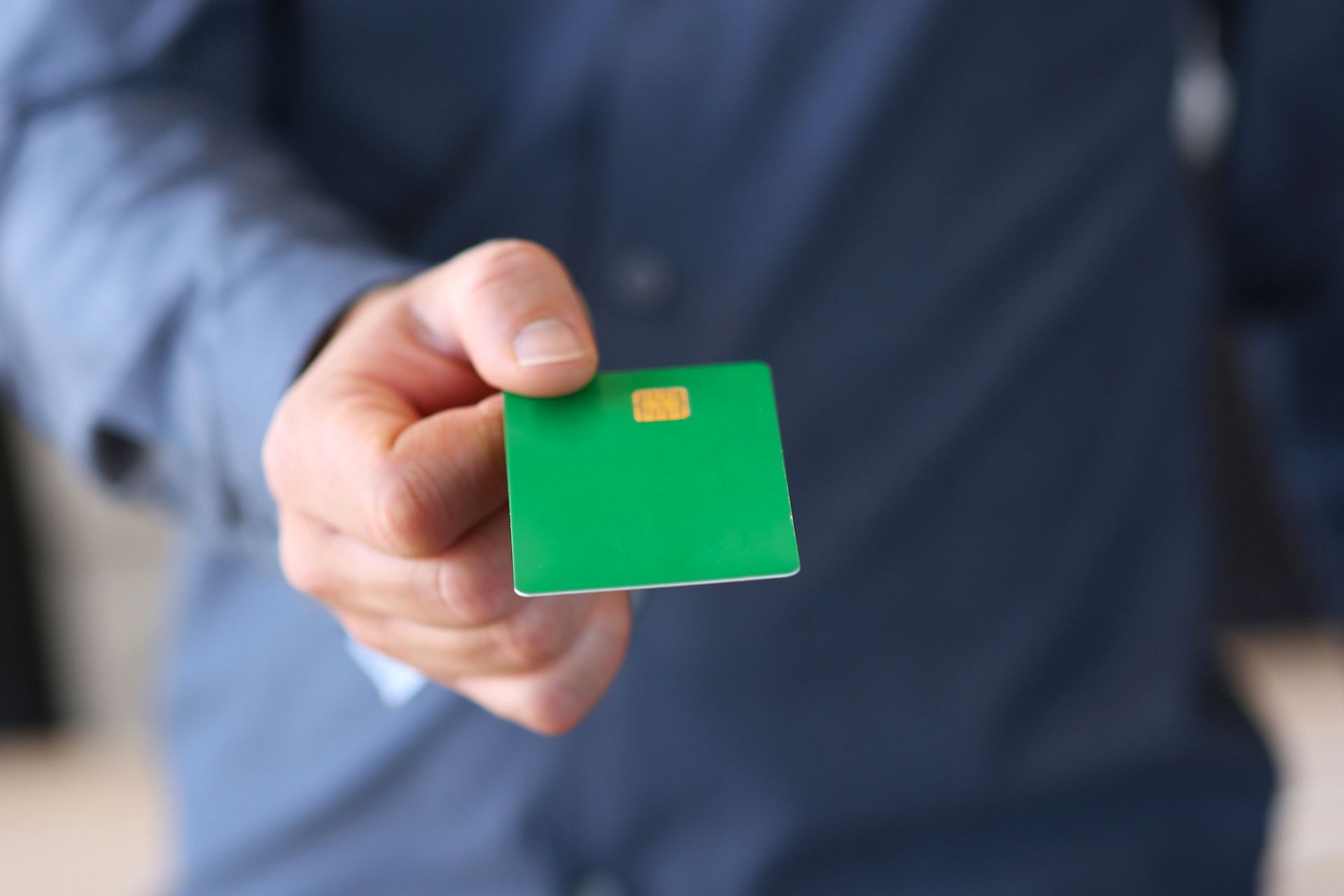 Main tenant une carte de crédit verte à puce dorée sur fond de chemise bleue floue