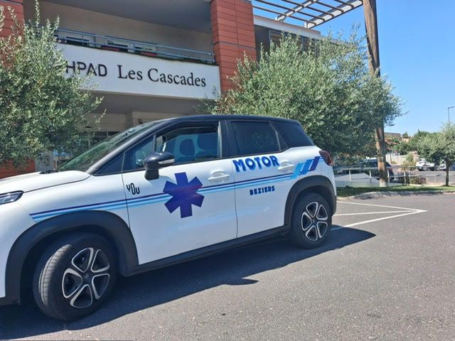 Un SUV d'urgence blanc et bleu est stationné devant l'établissement Les Cascades, dans une rue ensoleillée.