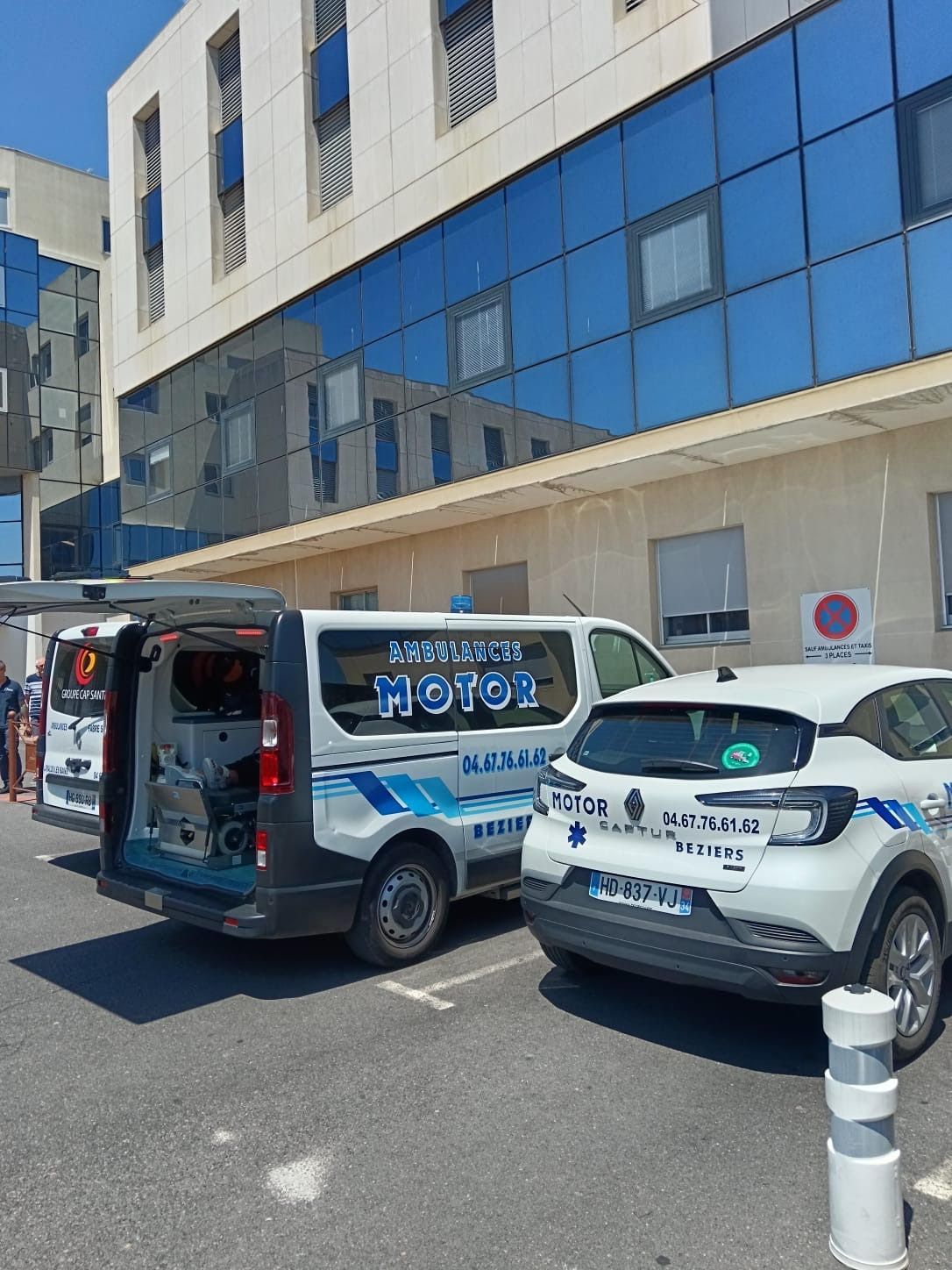 Une ambulance et un VSL garés à côté d'un bâtiment blanc vitré en plein jour.