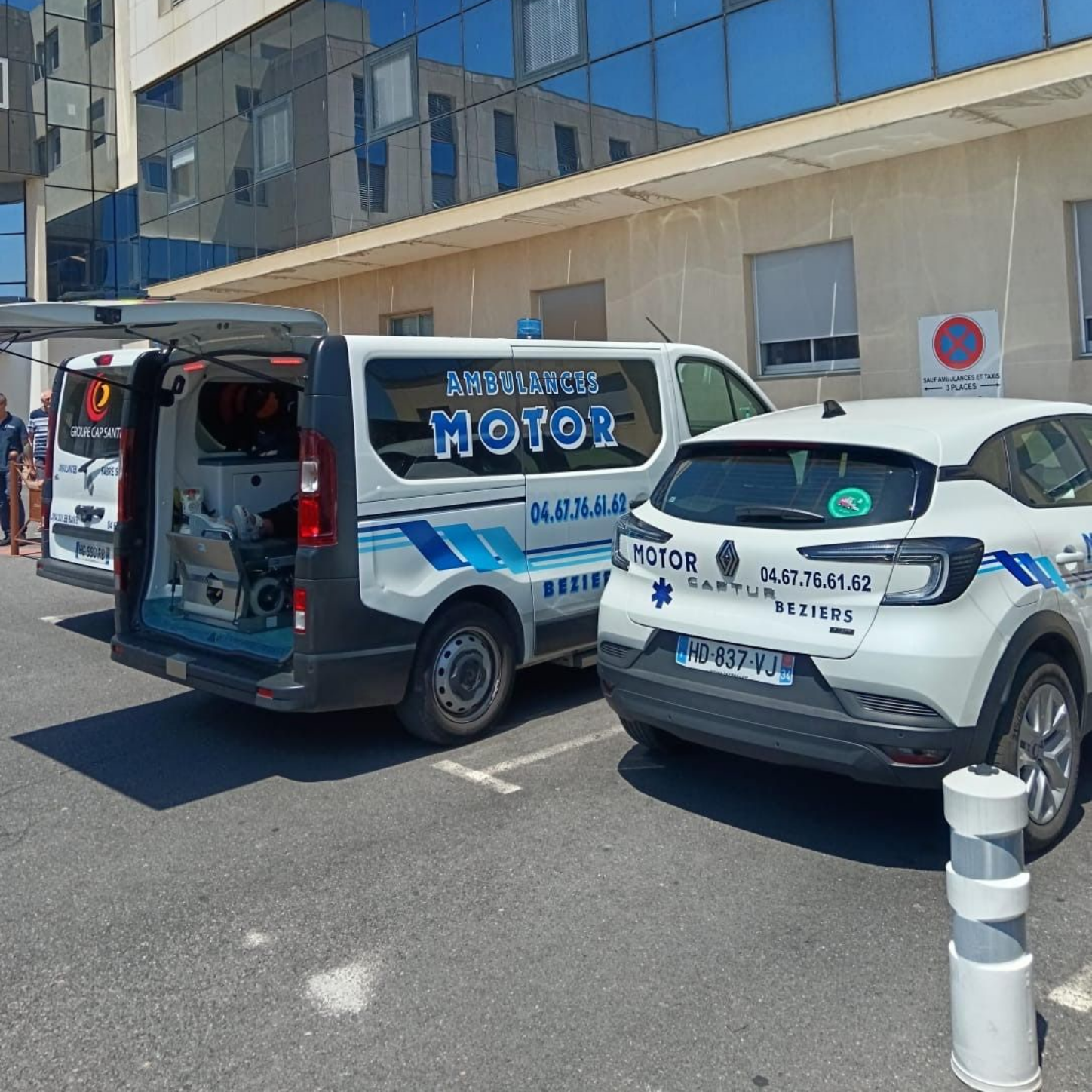 Deux fourgonnettes stationnées devant un bâtiment aux vitres bleues, dans une rue ensoleillée.