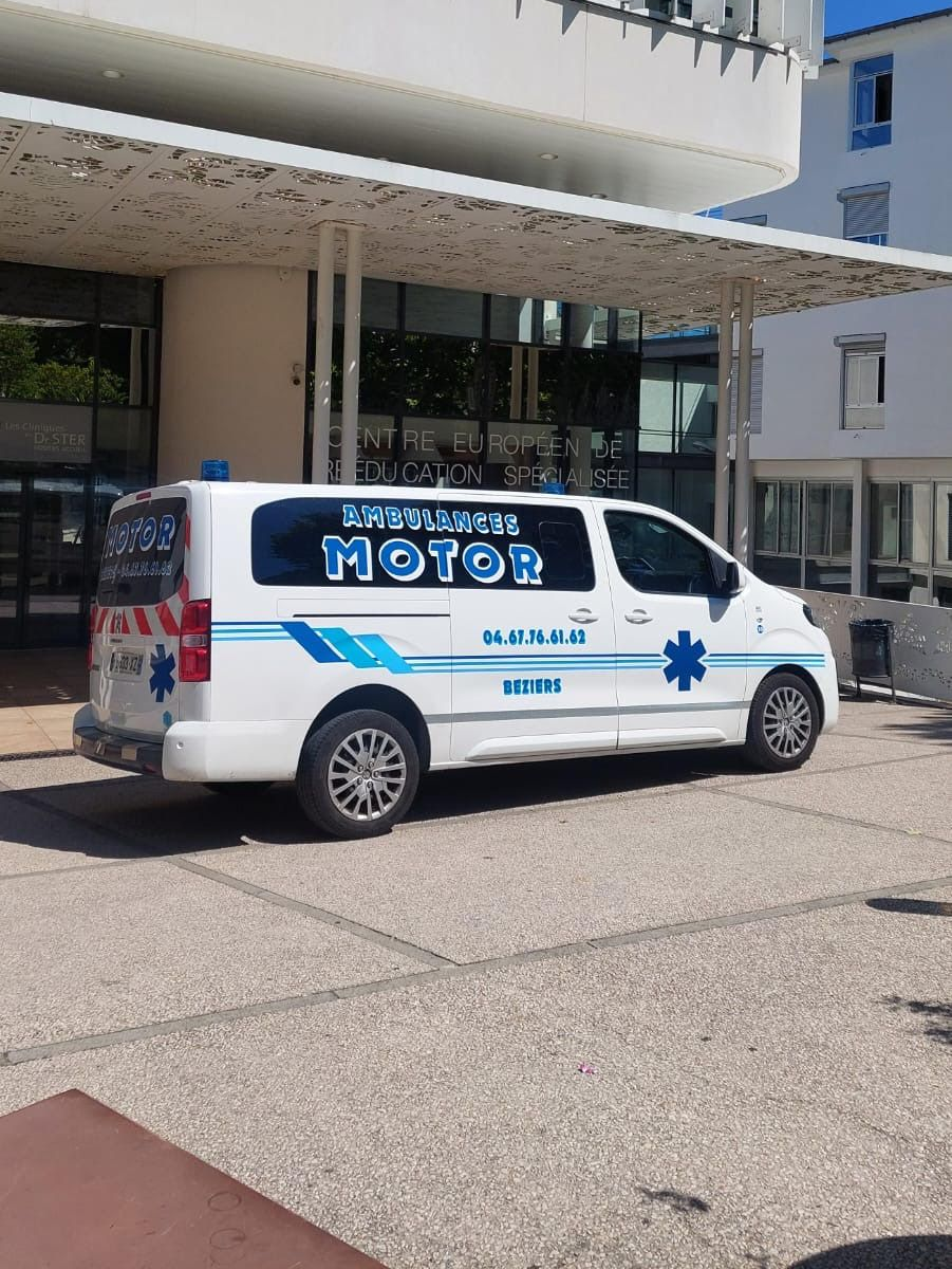Une ambulance blanche est garée devant l'entrée d'un bâtiment.