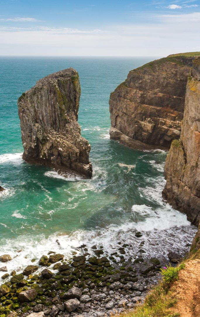 Rocky cliffs and sea stacks along a turquoise coast under a blue sky.
