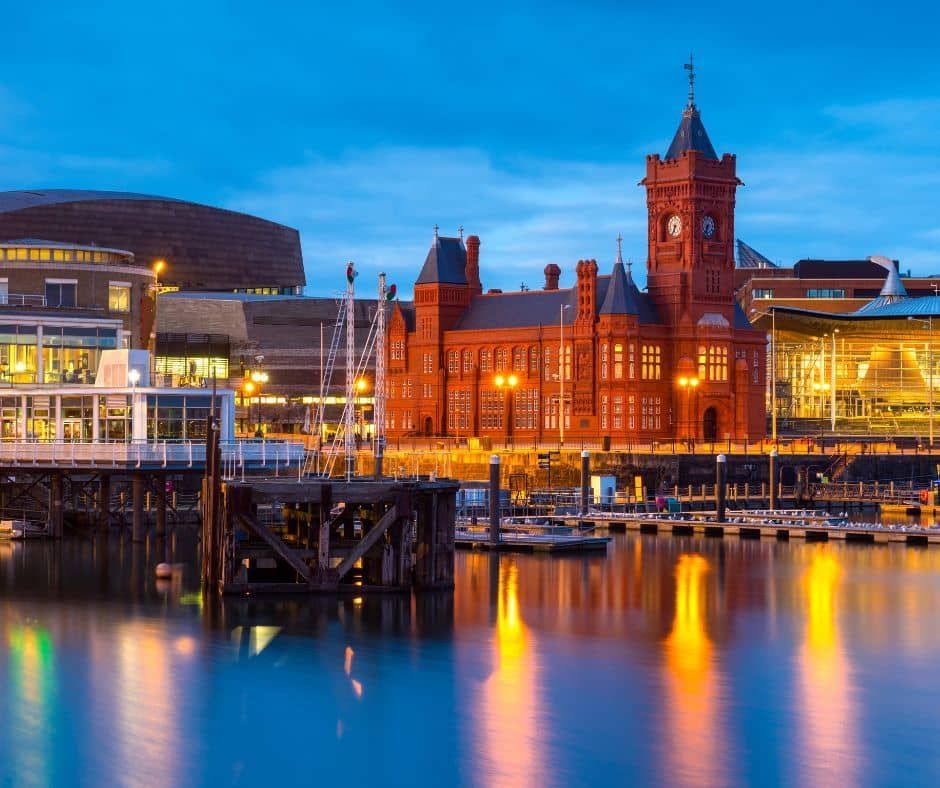 Cardiff Bay waterfront with the red brick Pierhead Building at dusk, reflecting in the water.