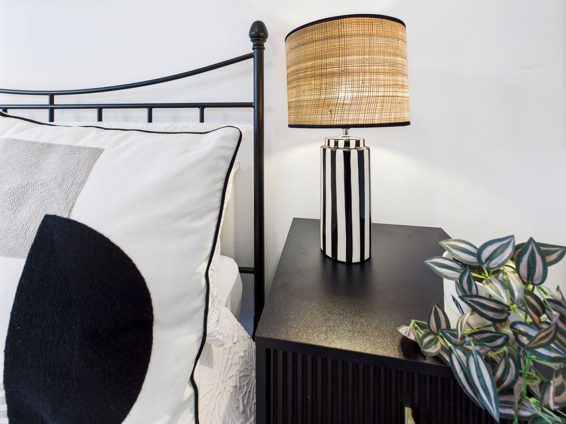 Bedroom scene with bed, nightstand, lamp, and decorative pillow. Black and white color scheme.