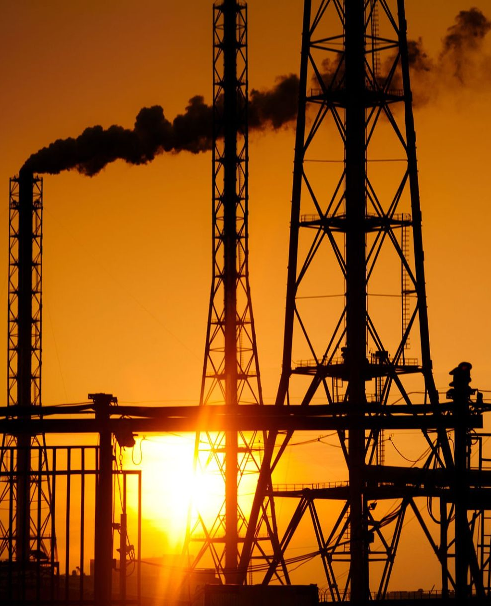 Smokestacks silhouetted against a golden sunset, billowing dark smoke, industrial setting.