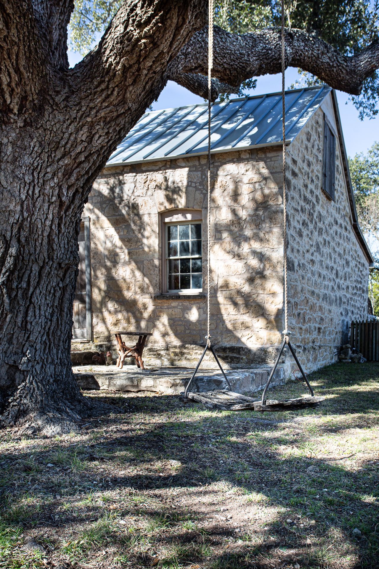 A swing is hanging from a tree in front of a stone building.