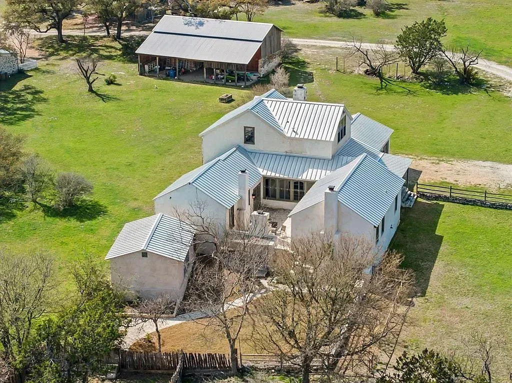 An aerial view of a house with a blue roof in the middle of a grassy field.